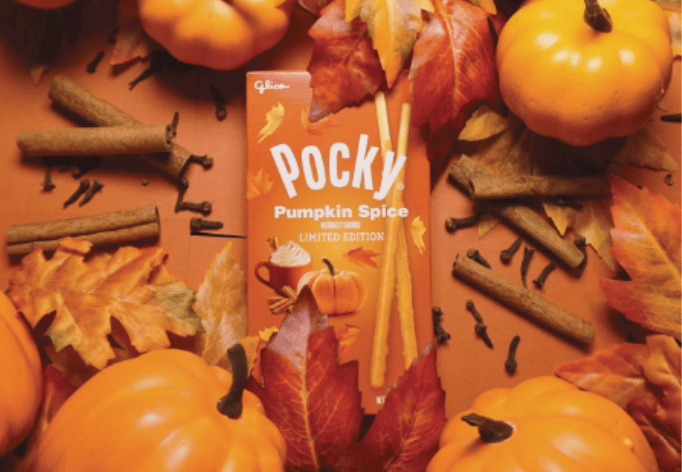 A box of Pocky Pumpkin Spice surrounded by fall leaves, pumpkins, and cinnamon sticks in orange background